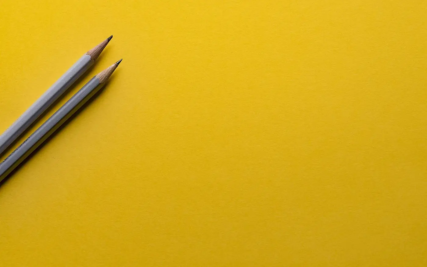 Two sharpened grey pencils lying on a plain yellow surface